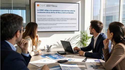 Empleados de oficina siguen en pantalla la noticia sobre la CNMC, con documentación de telecomunicaciones a su alrededor.