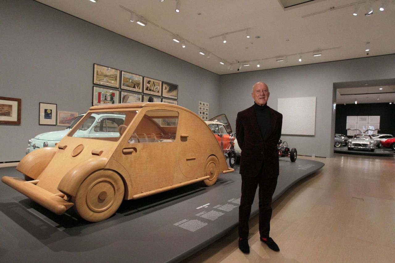 Norman Foster situado al lado del vehículo Voiture Minimum diseñado por Le Corbusier También en la misma sala localizado de espaldas al MINI seccionado por la mitad